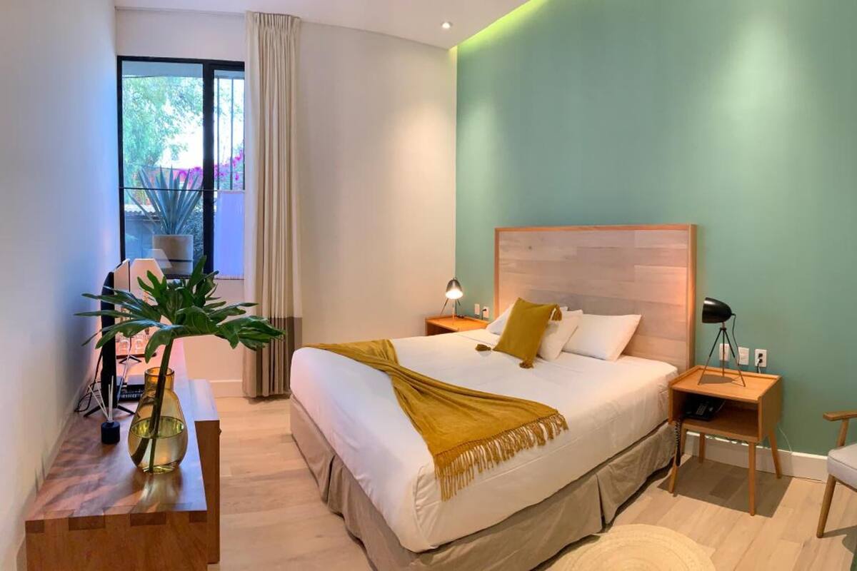 A bedroom with a bed, bedside table, lamp, chair, and a potted plant.