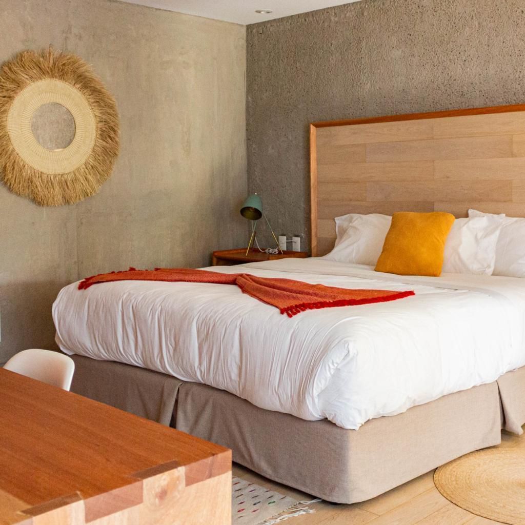 A modern hotel room with a large bed, a wooden headboard, a round wall decoration, a nightstand with a lamp, and a wooden table.