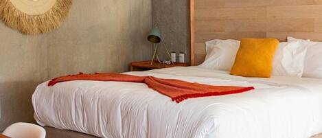 A modern hotel room with a large bed, a wooden headboard, a round wall decoration, a nightstand with a lamp, and a wooden table.