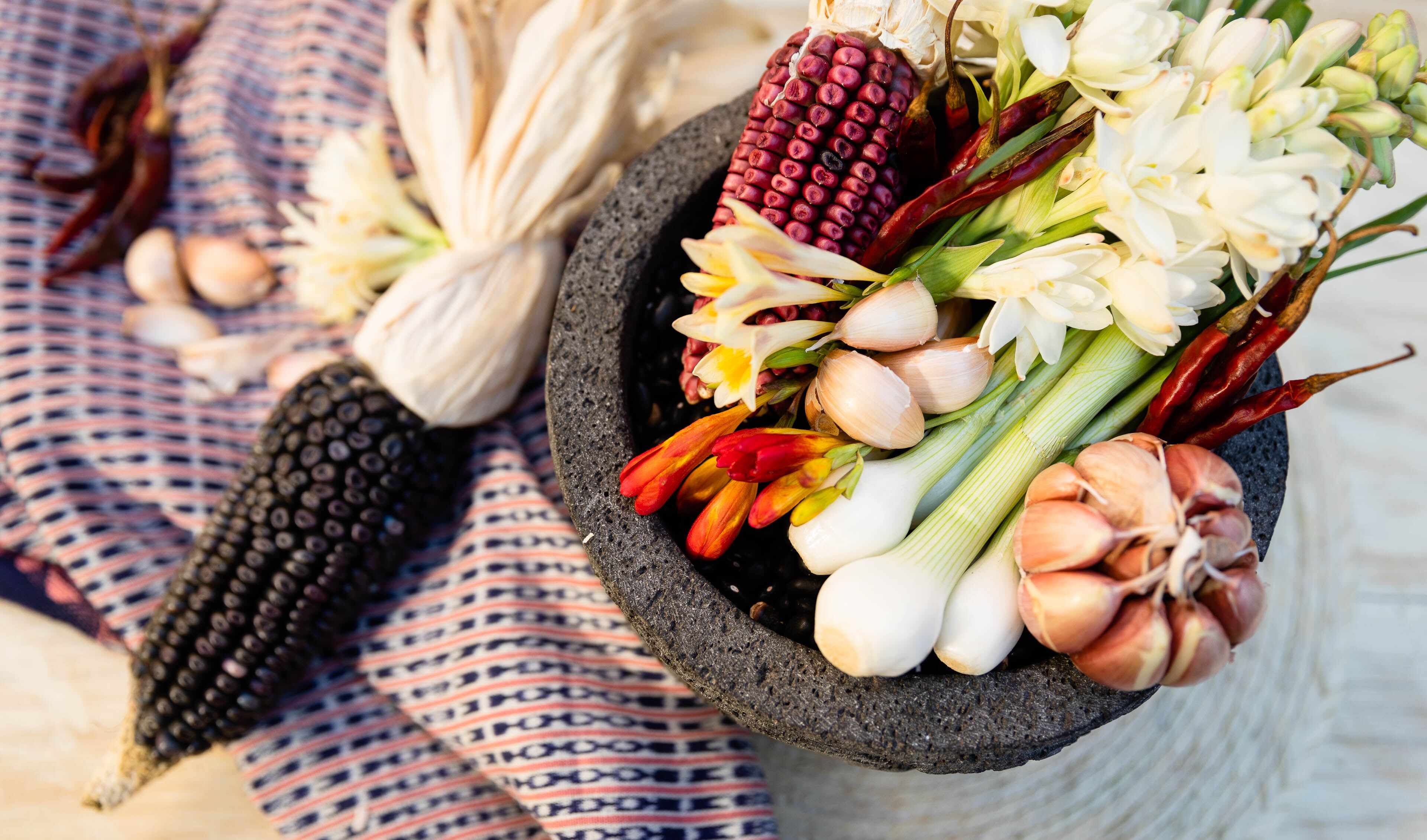 Un mortero de piedra lleno de ingredientes frescos como maíz, ajo y flores.