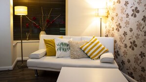 Un salon moderne avec un canapé blanc, des coussins décoratifs, une lampe sur pied et un vase rempli de fleurs rouges.