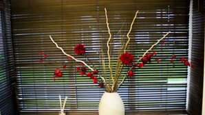 Una ventana con un jarrón blanco que contiene flores rojas y ramas, y un jarrón más pequeño con una vela.