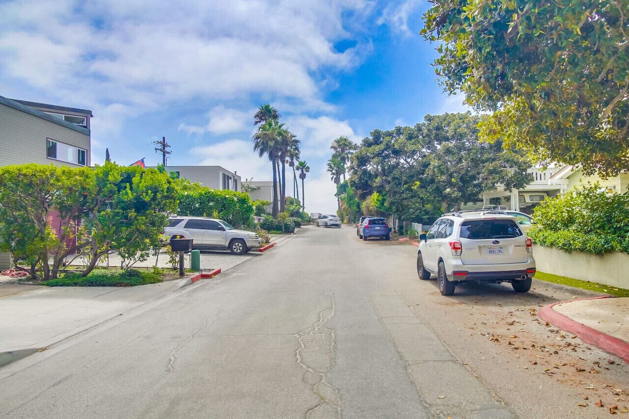 Rua residencial com carros estacionados, casas e árvores.