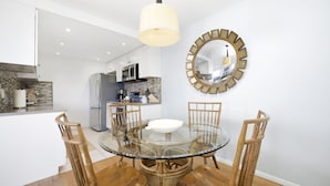 Een moderne keuken met een centraal eiland, een eethoek met een glazen tafel en houten stoelen, en een ronde spiegel aan de muur.