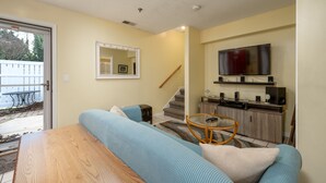 Un salon comprenant un canapé, une table basse, un téléviseur fixé au mur et un escalier menant à un autre niveau.