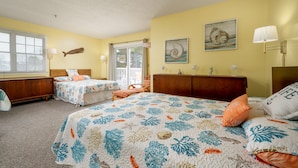 Une chambre avec deux lits, une tête de lit en bois, une fenêtre avec des stores et une porte donnant sur l’extérieur.