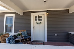 Eine Veranda mit einer weißen Tür, einer Fußmatte und zwei Holzstühlen mit Kissen.