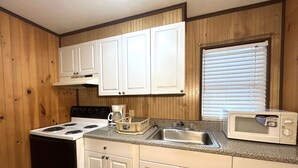 A compact kitchen with white cabinets, a stove, a coffee maker, a sink, and a microwave. - COASTAL BREEZE OCEAN CITY Wilmington terrace apartment 4 (Ocean City)