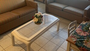 A cozy living room with two striped sofas, a glass coffee table with a floral centerpiece, and a ceiling fan. - COASTAL BREEZE OCEAN CITY Wilmington terrace apartment 4 (Ocean City)