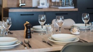 Una cocina moderna con armarios oscuros, un protector contra salpicaduras de madera y una zona de comedor dispuesta con platos, vasos y cubiertos.