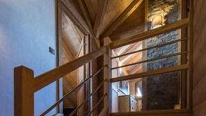 Una escalera de madera que lleva a una zona superior con una pared de piedra y una lámpara colgante.