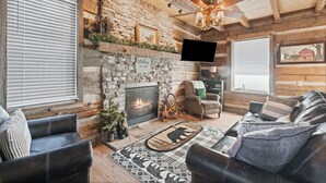 Ein gemütliches Blockhaus-Interieur mit Kamin, Ledersofas und einer Steinwand.
