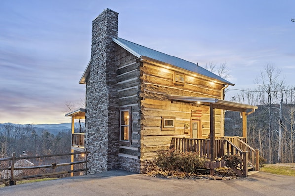 Une cabane en rondins avec une cheminée en pierre, une véranda en bois et une vue sur les montagnes environnantes.