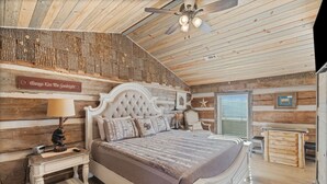 Ein Schlafzimmer mit Holzbalkendecke, einem Bett mit einer gepolsterten Kopfstütze, einem Nachttisch mit Lampe und einem Schild an der Wand.