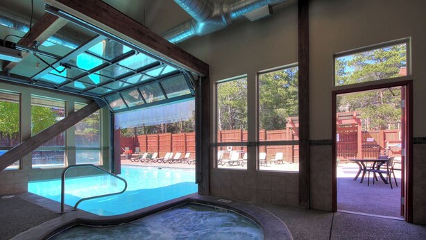 An indoor swimming pool with a glass ceiling, lounge chairs, and a view of the outdoor area.