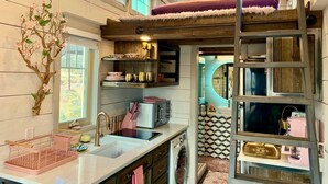 A compact kitchen with a built-in washing machine, a sink, and a wooden ladder leading to a loft bed. - Mother Eve Tiny House (Washington County)