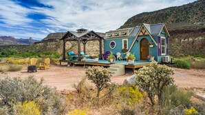 A rustic cabin with a porch, outdoor seating, and potted plants. - Mother Eve Tiny House (Washington County)
