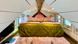 A cozy attic bedroom with a green bed, pink and white pillows, a fluffy rug, and a wooden ceiling. - Mother Eve Tiny House (Washington County)