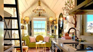 A cozy kitchen with a green sofa, a chandelier, and a view of the outdoors. - Mother Eve Tiny House (Washington County)
