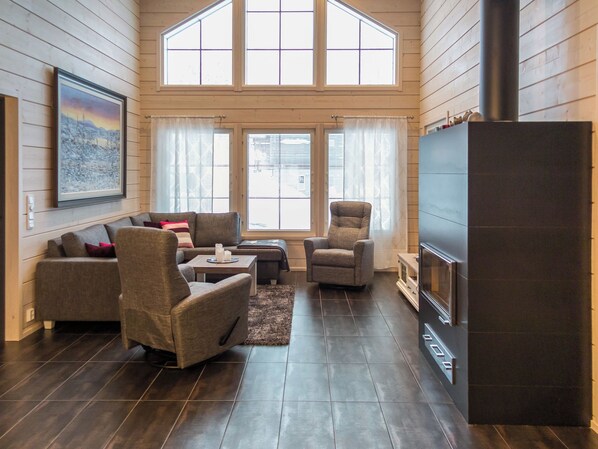 A modern living room with a fireplace, wooden flooring, and large windows.