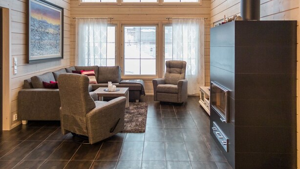 A cozy living room with a fireplace, wooden walls, and large windows.