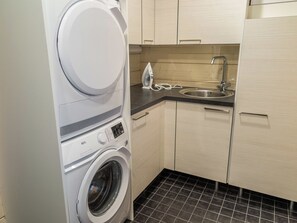 Un espace buanderie compact comprenant un lave-linge à chargement frontal, un sèche-linge, une petite planche à repasser et un évier.