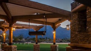 Un espace extérieur aménagé en terrasse, avec des piliers en pierre, une balançoire et une vue sur un terrain de golf.
