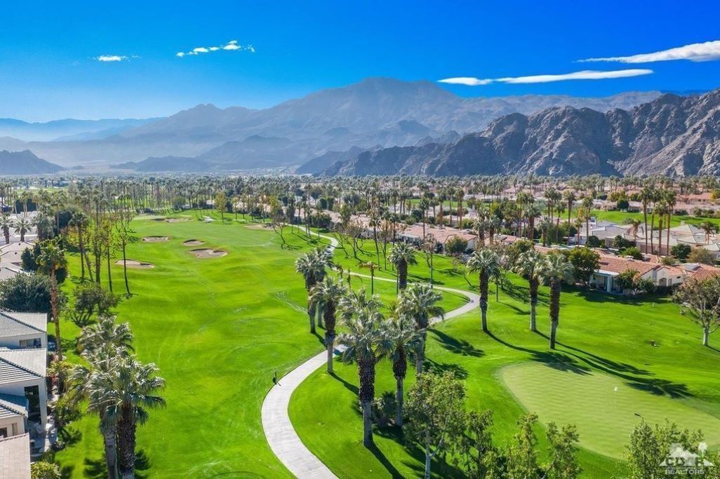 Un campo de golf con un camino despejado, palmeras y montañas al fondo.