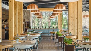 Un restaurant avec des poutres en bois, de grandes suspensions en cuivre et une vue sur les arbres à travers de larges fenêtres.