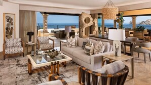Un salón amplio con un sofá grande, sillones, una mesa de centro y un comedor. Un ventanal ofrece vistas al océano.