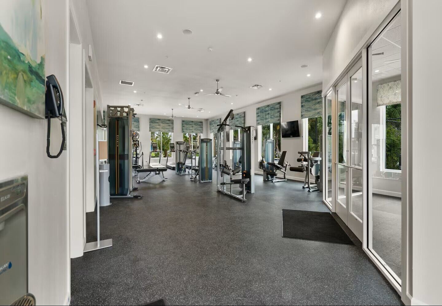 A modern gym with various exercise equipment, large windows, and a clean, well-lit interior.