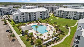 A multi-story residential building with a central swimming pool surrounded by lounge chairs and palm trees.
