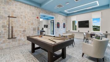 A billiards room with a pool table, chairs, and a TV.