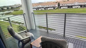 Un balcón con dos sillas y una mesa pequeña, con vistas a una zona cubierta de césped y un cuerpo de agua.