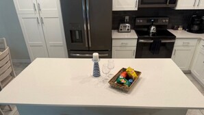 Una cocina con una isla central, armarios blancos, electrodomésticos de acero inoxidable y una zona de estar con dos sillas.