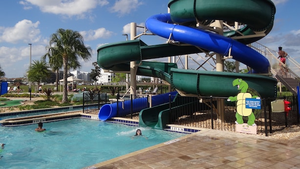 Parque acuático con una estructura de toboganes de varios niveles, piscina y torre de salvavidas.