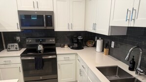 Una cocina moderna con armarios blancos, horno de acero inoxidable, microondas, tostadora, cafetera y pileta.