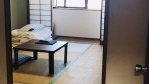 Una stanza tradizionale giapponese con pavimento in tatami, un letto basso, un tavolino e una porta scorrevole.
