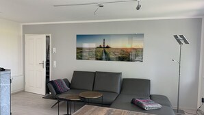 A modern living room with a grey sofa, a coffee table, and a painting of a lighthouse. - Beacon (Vollerwiek)
