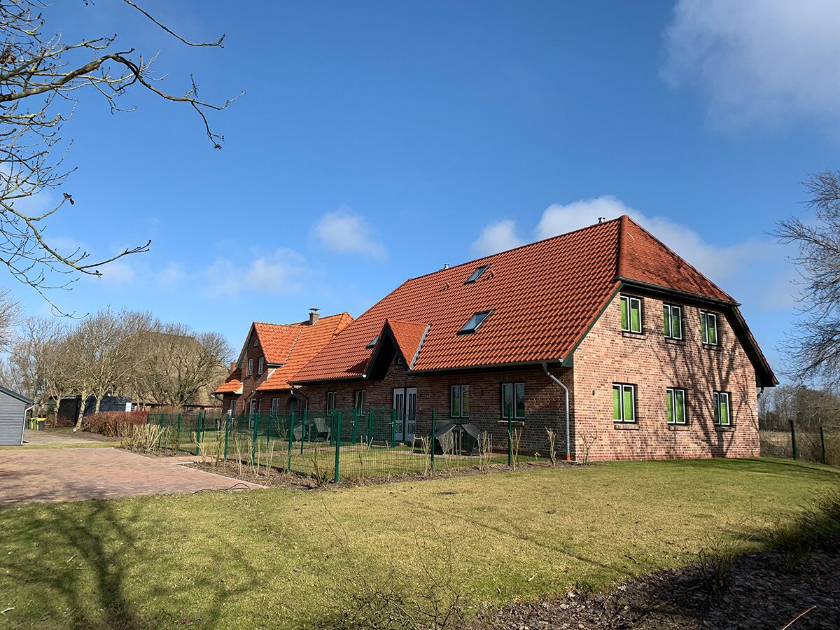 A two-story brick house with a red-tiled roof, green shutters, and a well-maintained lawn.