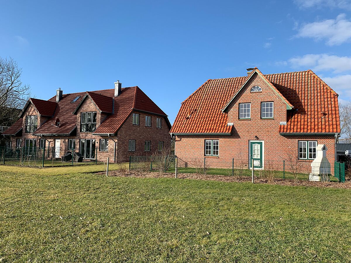 Two brick houses with red-tiled roofs and a grassy field in front.