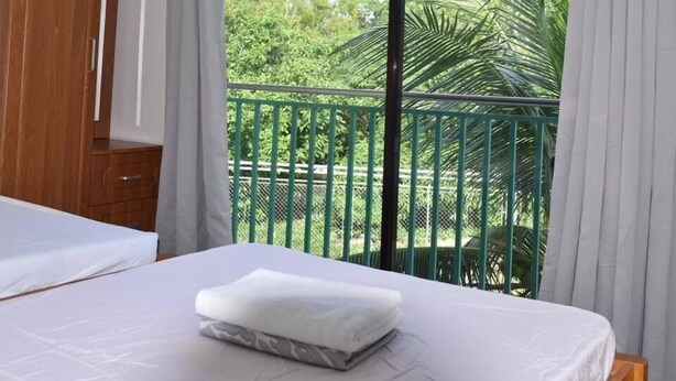 A bedroom with a bed, a wooden wardrobe, and a balcony with a green railing and palm trees. - Charlina Rooms for Rent (Panglao)