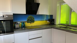 A modern kitchen with white cabinets, a black range hood, a built-in microwave, and a window with green blinds. - Bird Migration - (Vollerwiek)