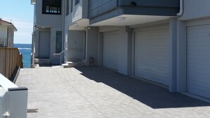 A modern residential building with a covered driveway, a visible entrance, and a view of the ocean. - Beachfront Penthouse The Entrance (The Entrance)