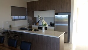 A modern kitchen with a central island, stainless steel appliances, and a vase with flowers. - Beachfront Penthouse The Entrance (The Entrance)
