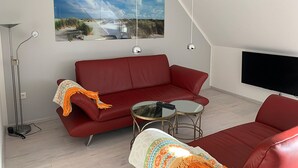 A modern living room with a red sofa, a glass coffee table, and a floor lamp. - Dünentraum, Ferienwohnung in "De Feerjenhusen" am Haubarg von Vollerwiek (Vollerwiek)