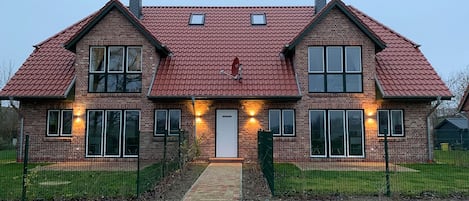 A two-story house with a red-tiled roof, brick exterior, and a front entrance with a small porch.