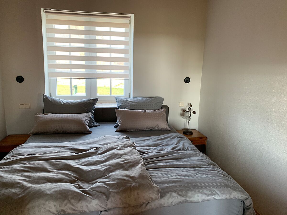 A bedroom with a bed, pillows, a nightstand, and a window with blinds.