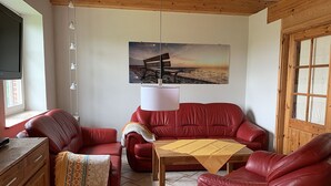Un salon chaleureux avec des canapés en cuir rouge, une table basse en bois et un tableau représentant une scène de plage accroché au mur.