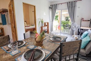 A dining table set with plates, glasses, and chopsticks, a pineapple centerpiece, and a fan in the background. - Enda Lanta Bungalows (Ko Lanta)
